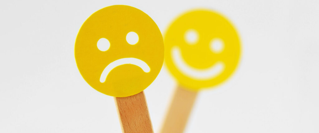 Faccia con espressione negativa davanti a una faccina sorridente sfocata - Concetto di emozione negativa